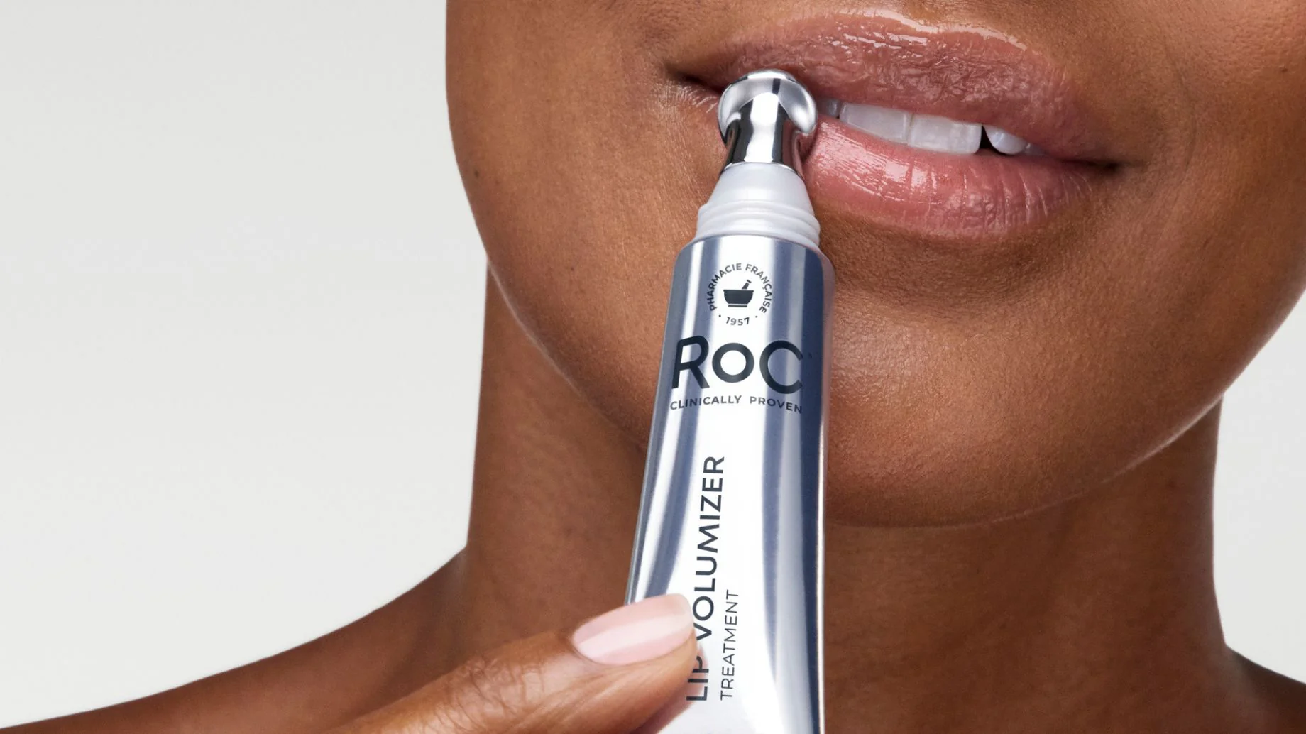 Person using a ROC lip volumizer on their lips with a plain background