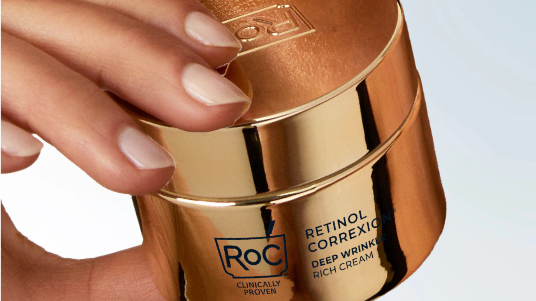 Gold container of Roc Retinol Correxion Deep Wrinkle Rich Cream held by a hand.